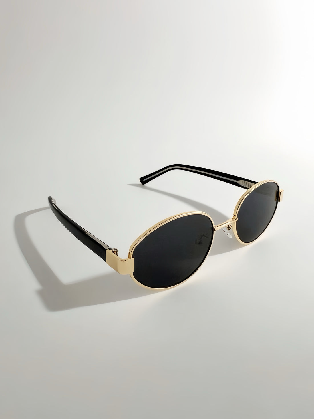Sunglasses with gold frame and black lenses on a light gray background