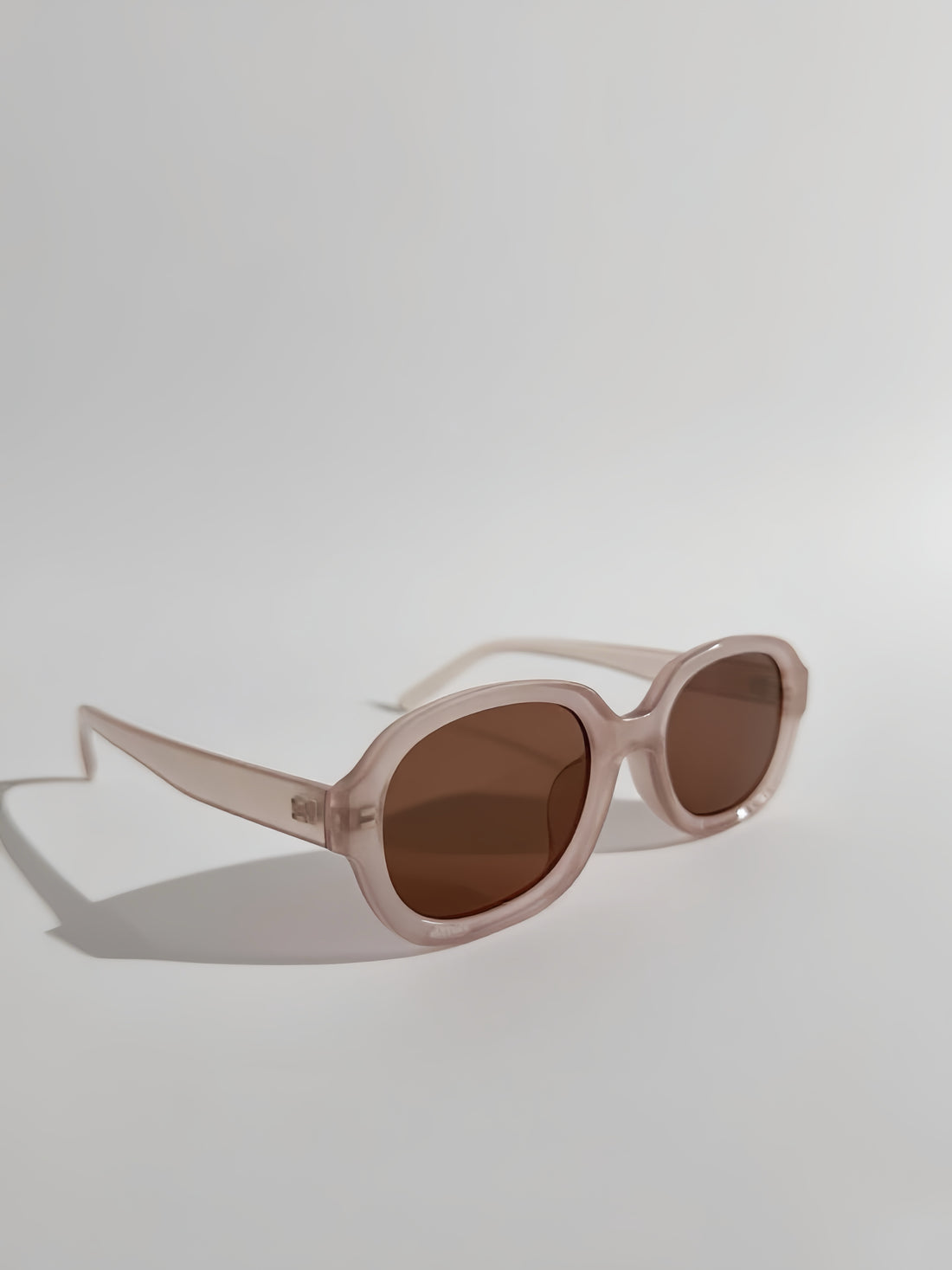 Sunglasses with a clear frame and brown lenses on a light gray background