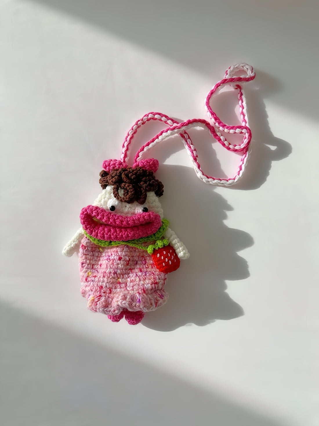 Crocheted character with pink dress and red strawberry on a white background