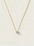 Gold necklace with a small round pendant on a light beige background