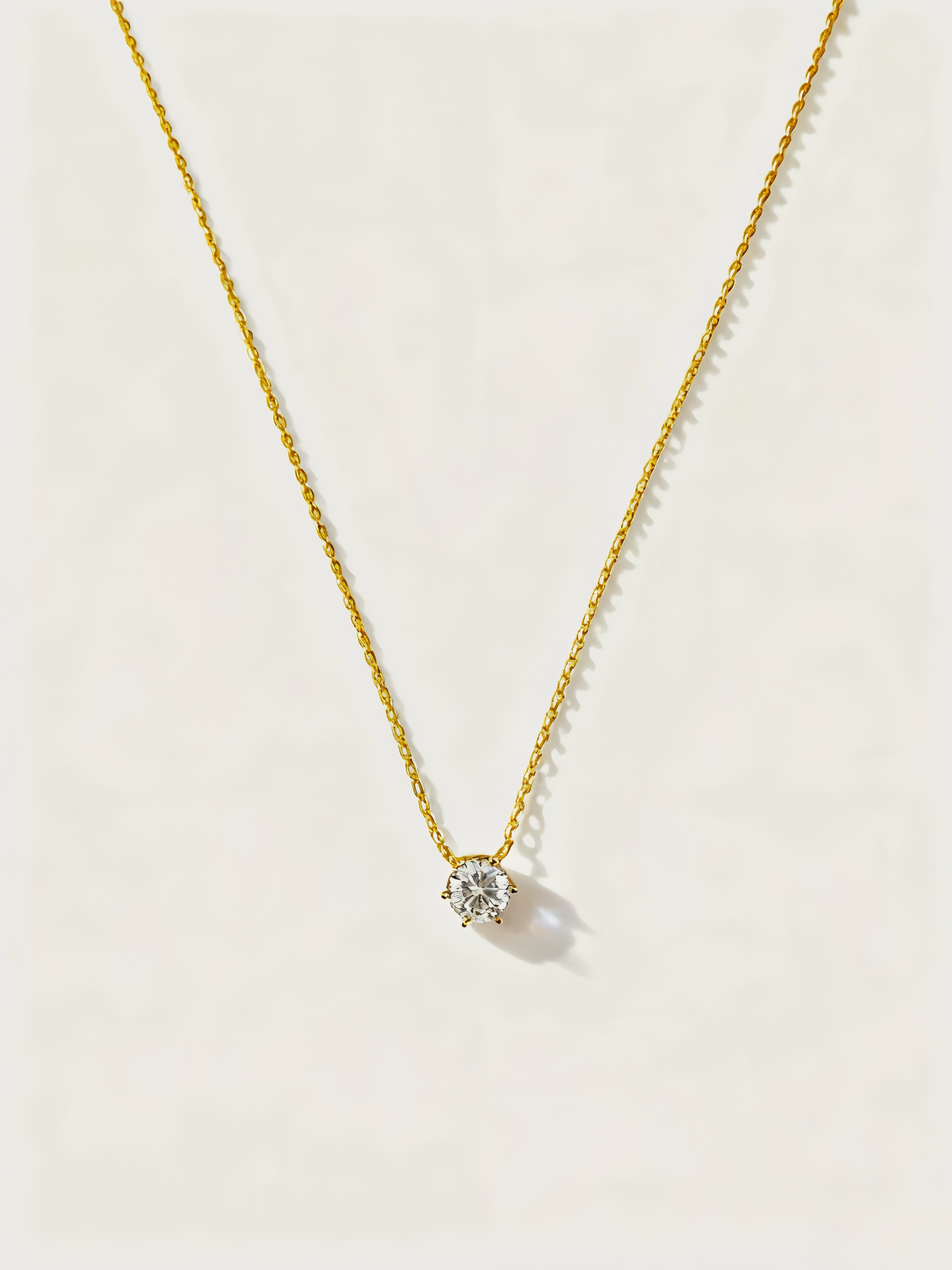 Gold necklace with a small round pendant on a light beige background