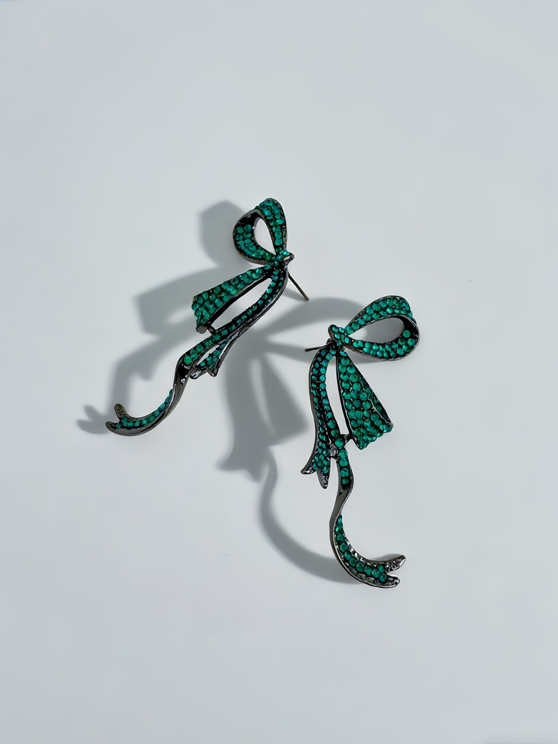Pair of green bow-shaped earrings on a light gray background