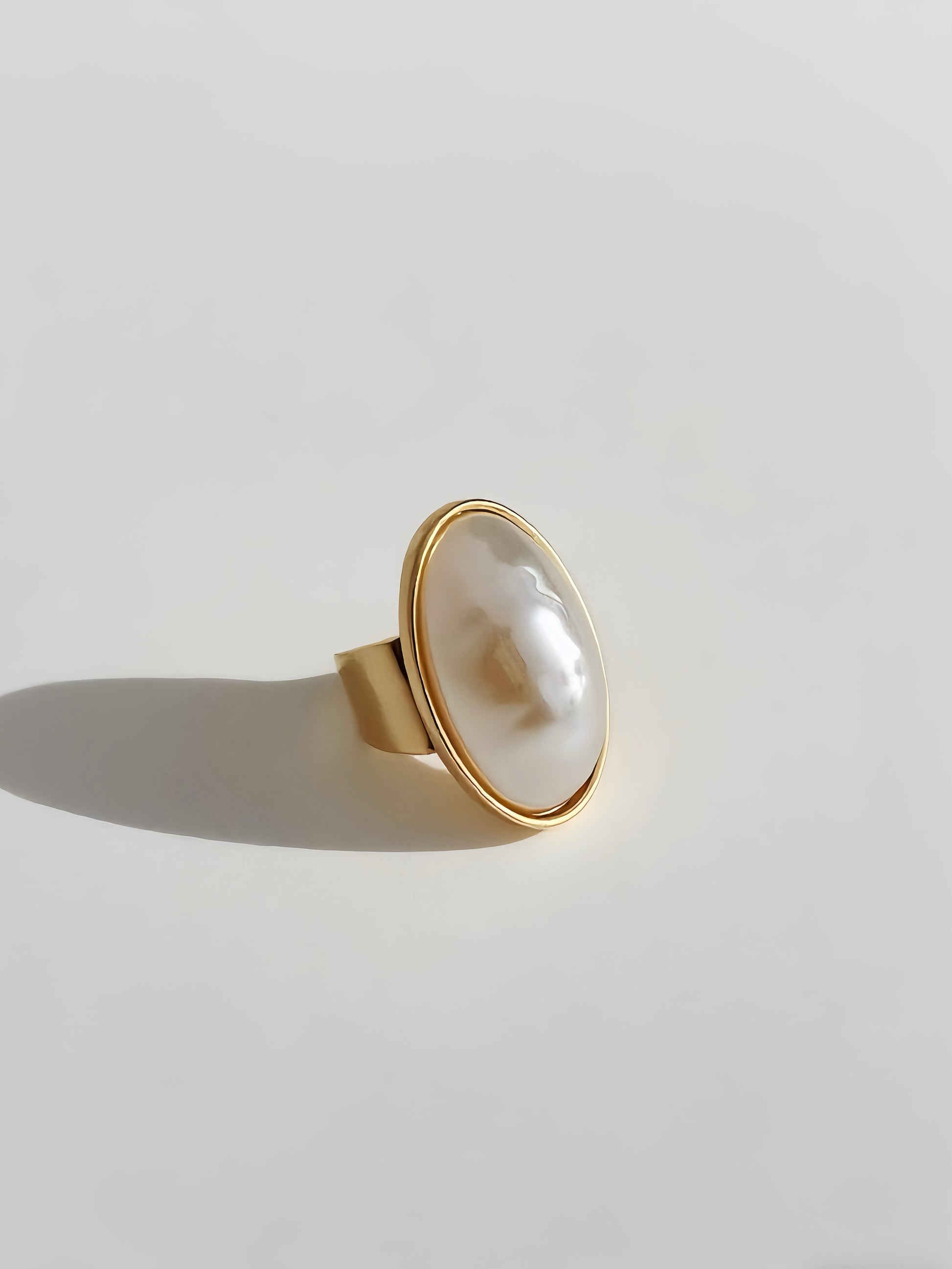 Gold ring with a large pearl on a light gray background